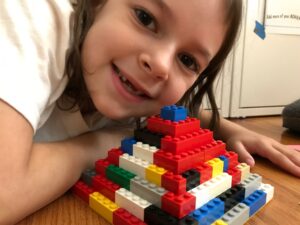 A young girl leans over a LEGO pyramid with a gap-toothed smile