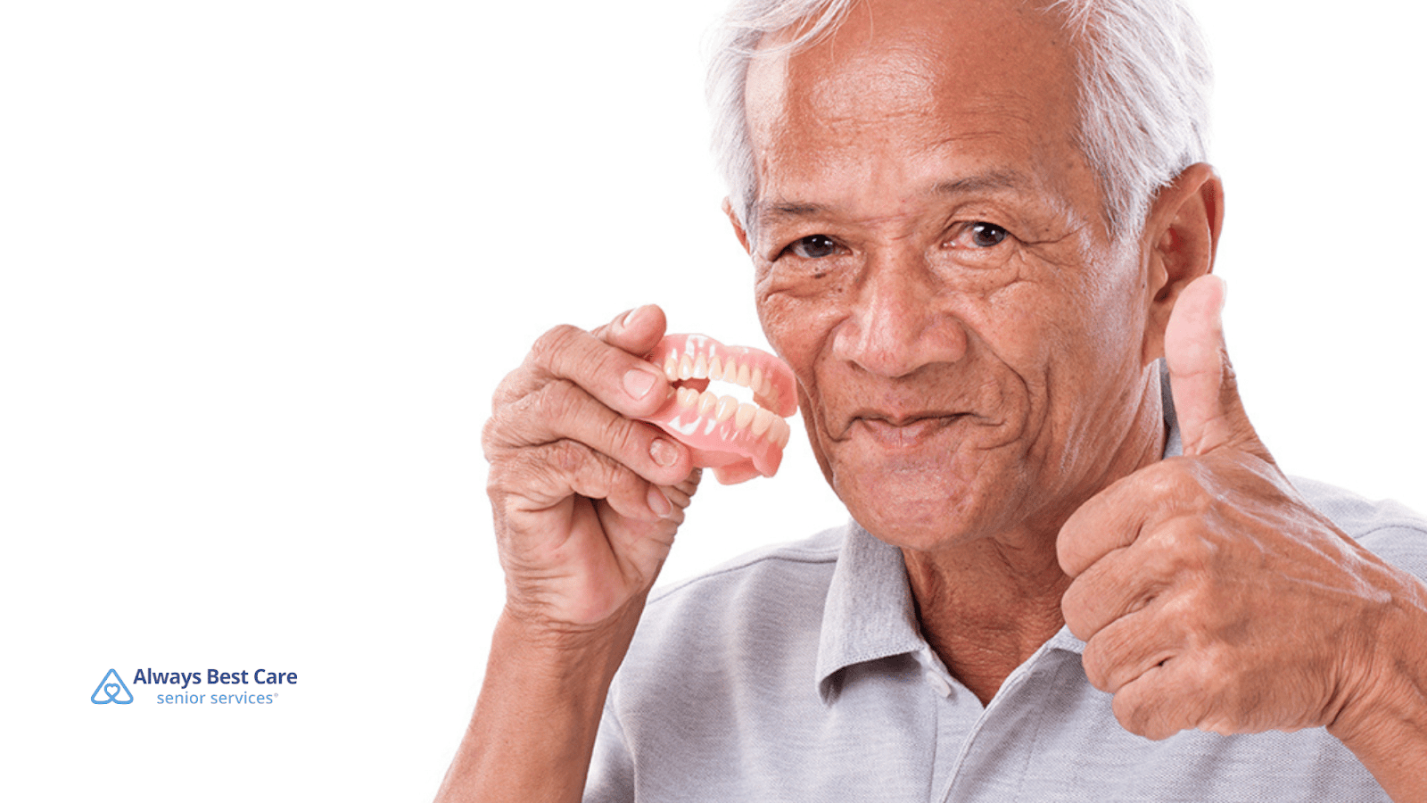 This is an image of a senior man holding a denture while giving the thumbs-up