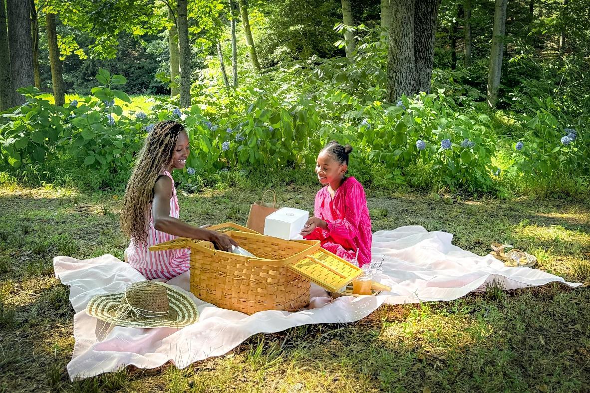 Two girls sitting on a blanket in the woods

Description automatically generated