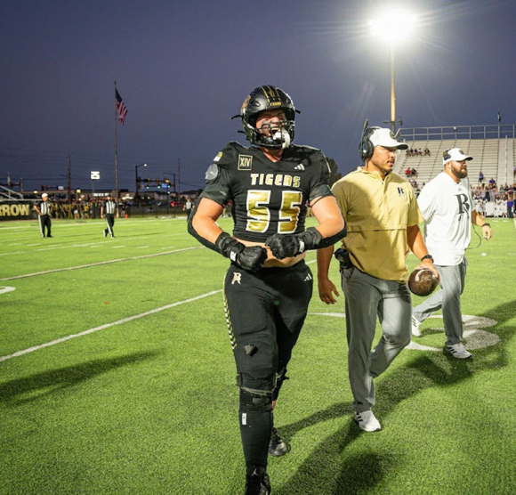 A football player walking on a field

Description automatically generated