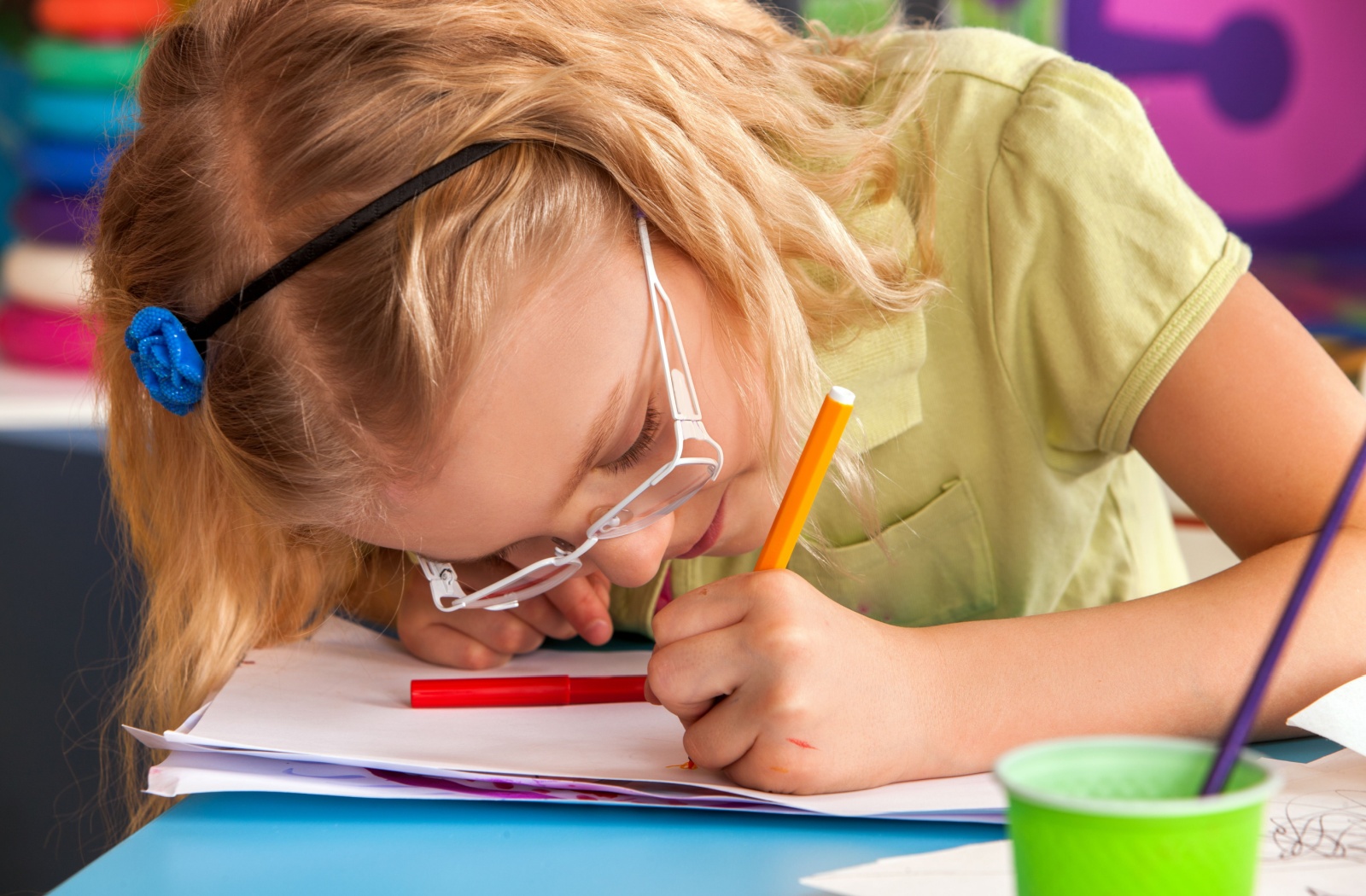 A child wearing glasses leans closely over a coloring book to see better.