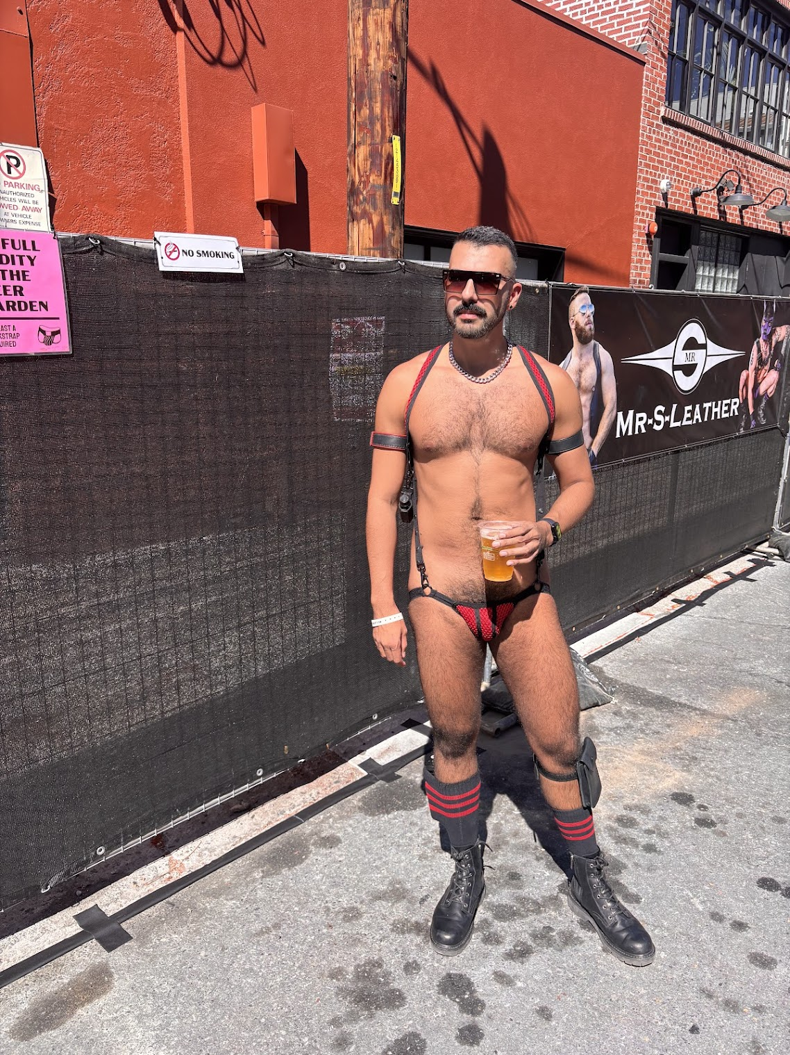 gay xxx porn model Phil standing in black and red harness shirtless with beer at the beer gardens sponsored by mr s leather during folsom street fair 2024