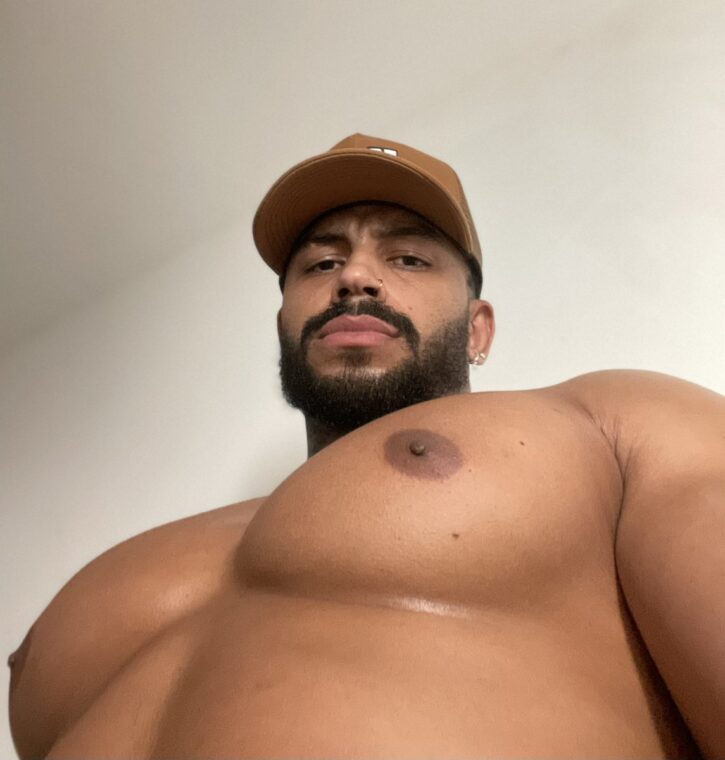 gay xxx onlyfans content creator Lipe Scorpio taking a low angle shirtless gay male selfie for gay porn content in brown baseball hat