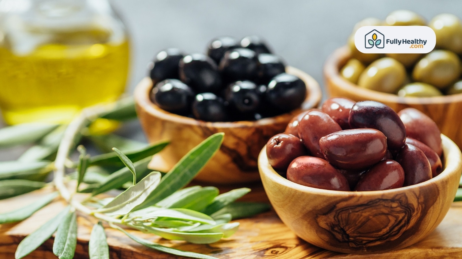 Assorted olives in wooden bowls with olive oil and leaves