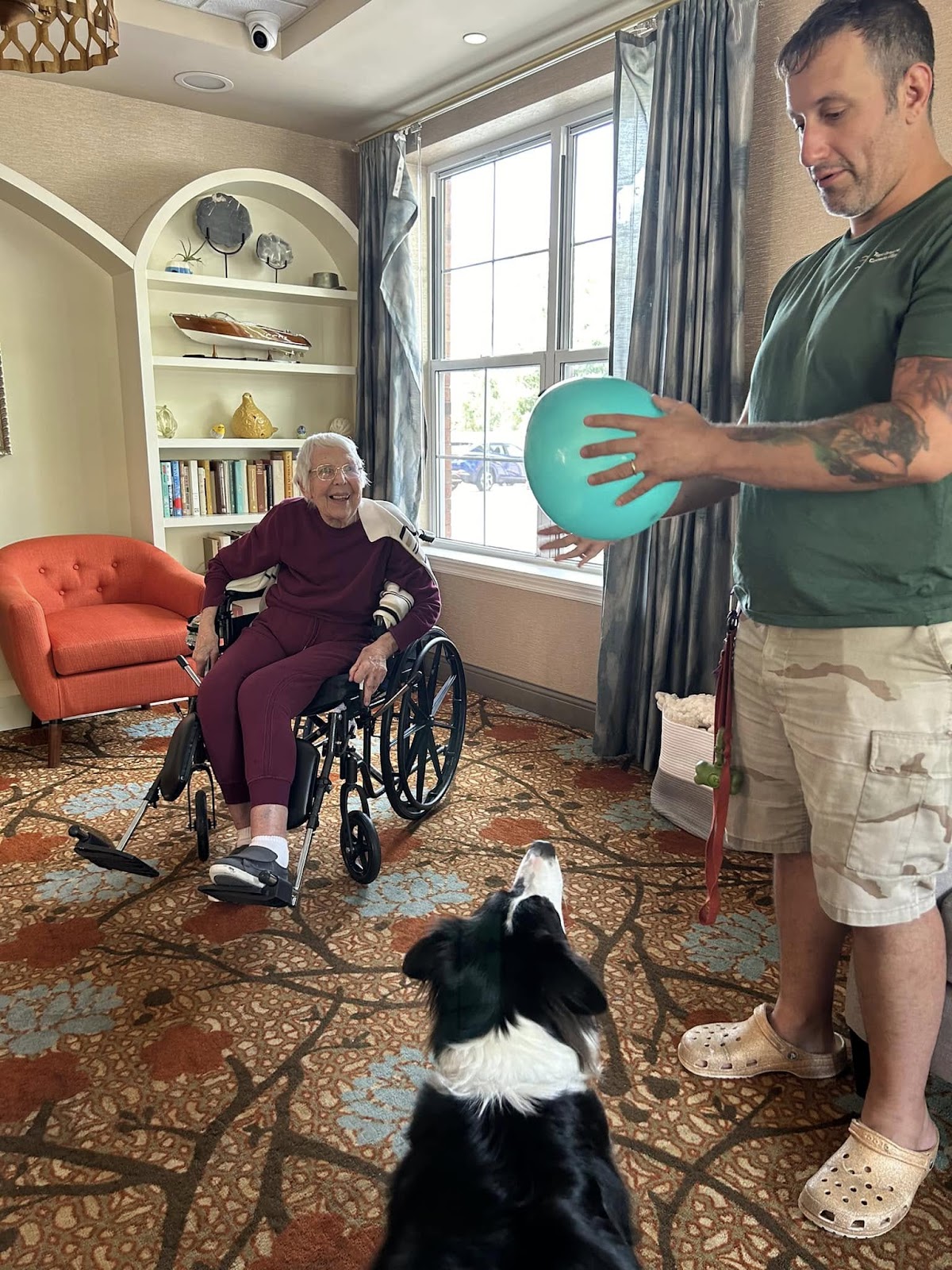 A picture of an elderly woman smiling with a dog and its owner nearby