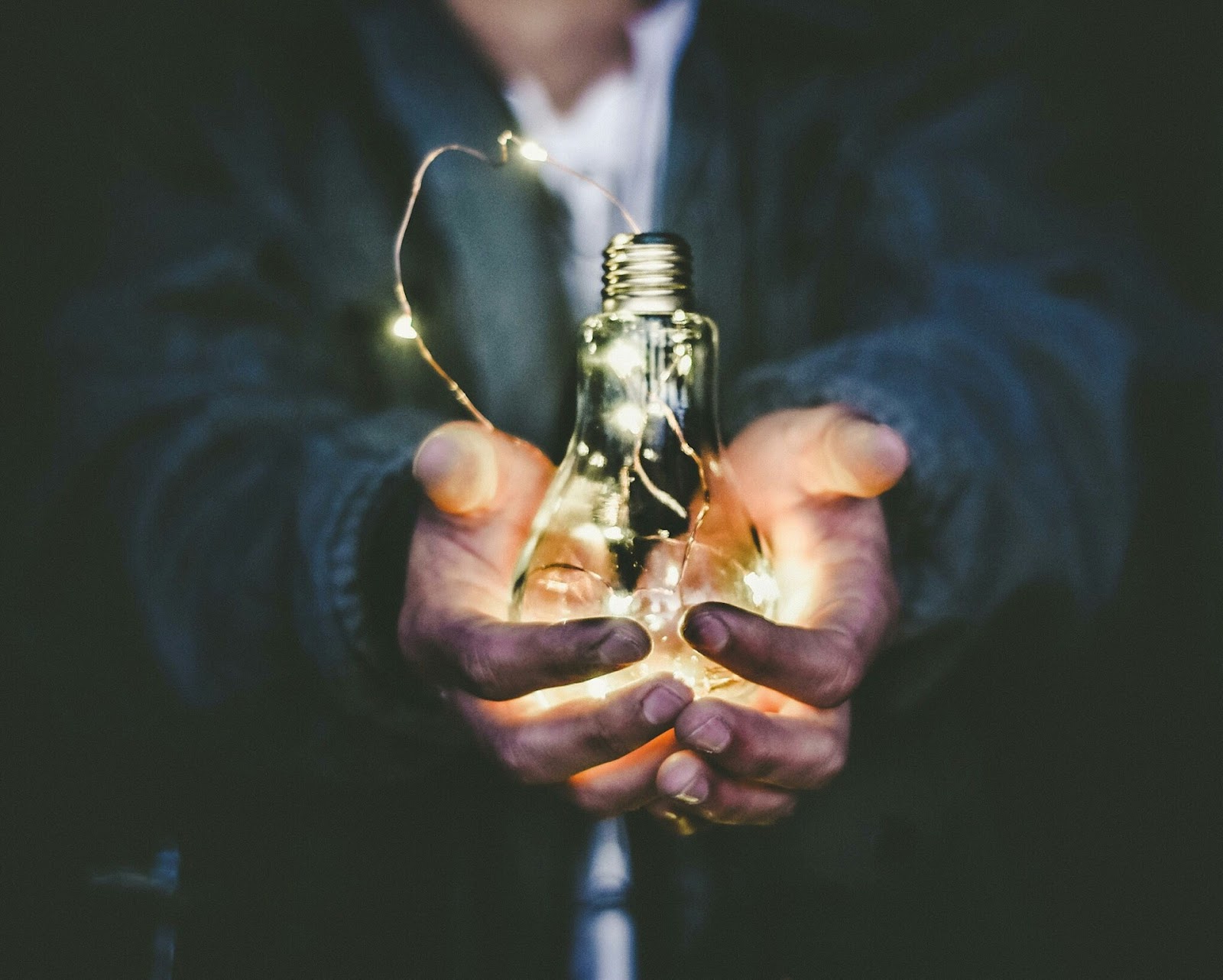 Person holding a glowing lightbulb wrapped in string lights, symbolizing bright ideas to run successful meetings.