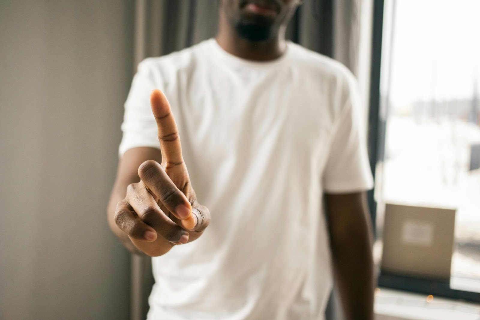 A man in a white t-shirt holds out a finger as if to say 'no'.