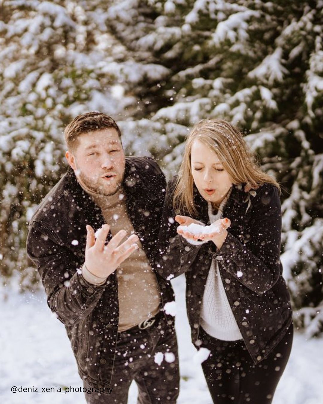 winter engagement photos a cheerful couple blows snow from their hands in the forest