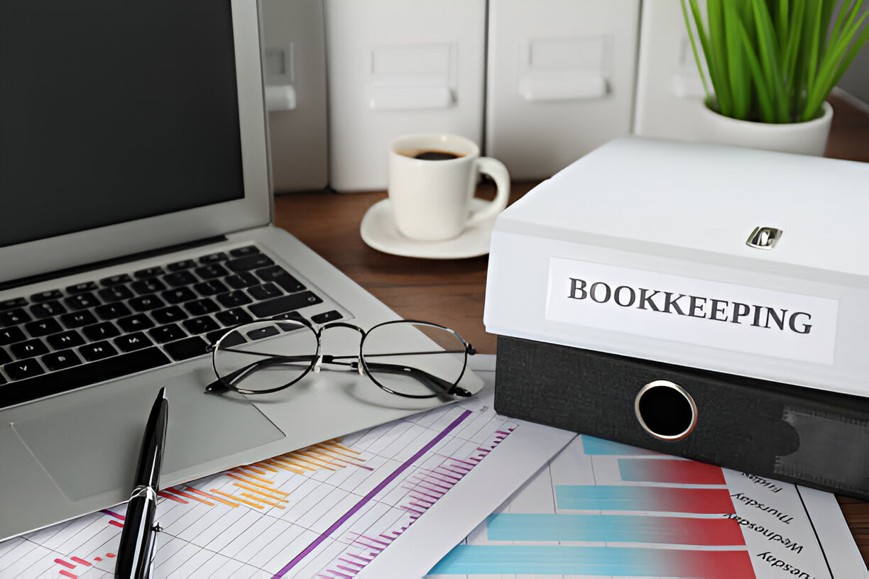 A laptop, eyeglasses, and a binder labeled 'Bookkeeping' on a desk, representing the importance of accurate bookkeeping for financial management.