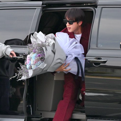 This contains an image of BTS Jin coming out of a car and aholding a flower