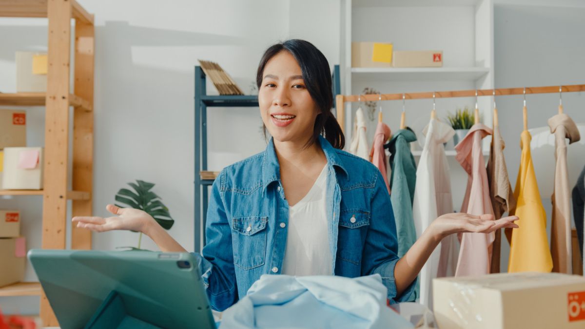 A young female online seller is gesturing while speaking in front of a tablet.