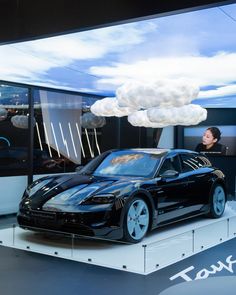 This contains an image of BLACKPINK Jennie Porsche Taycan  black sports car is on display in front of a cloud like object that appears to be floating