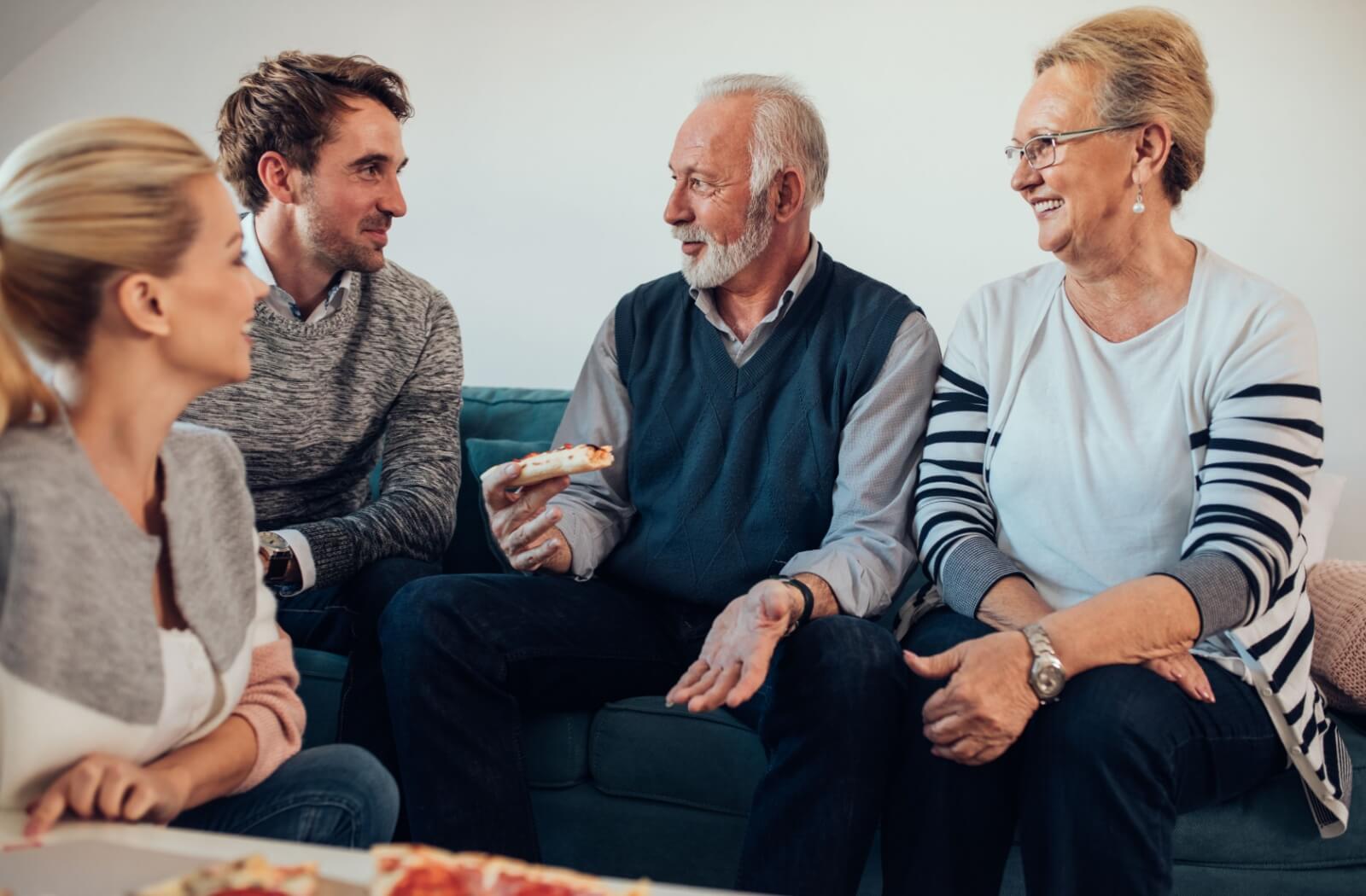 A senior couple and their adult children enjoy time chatting together over a meal.