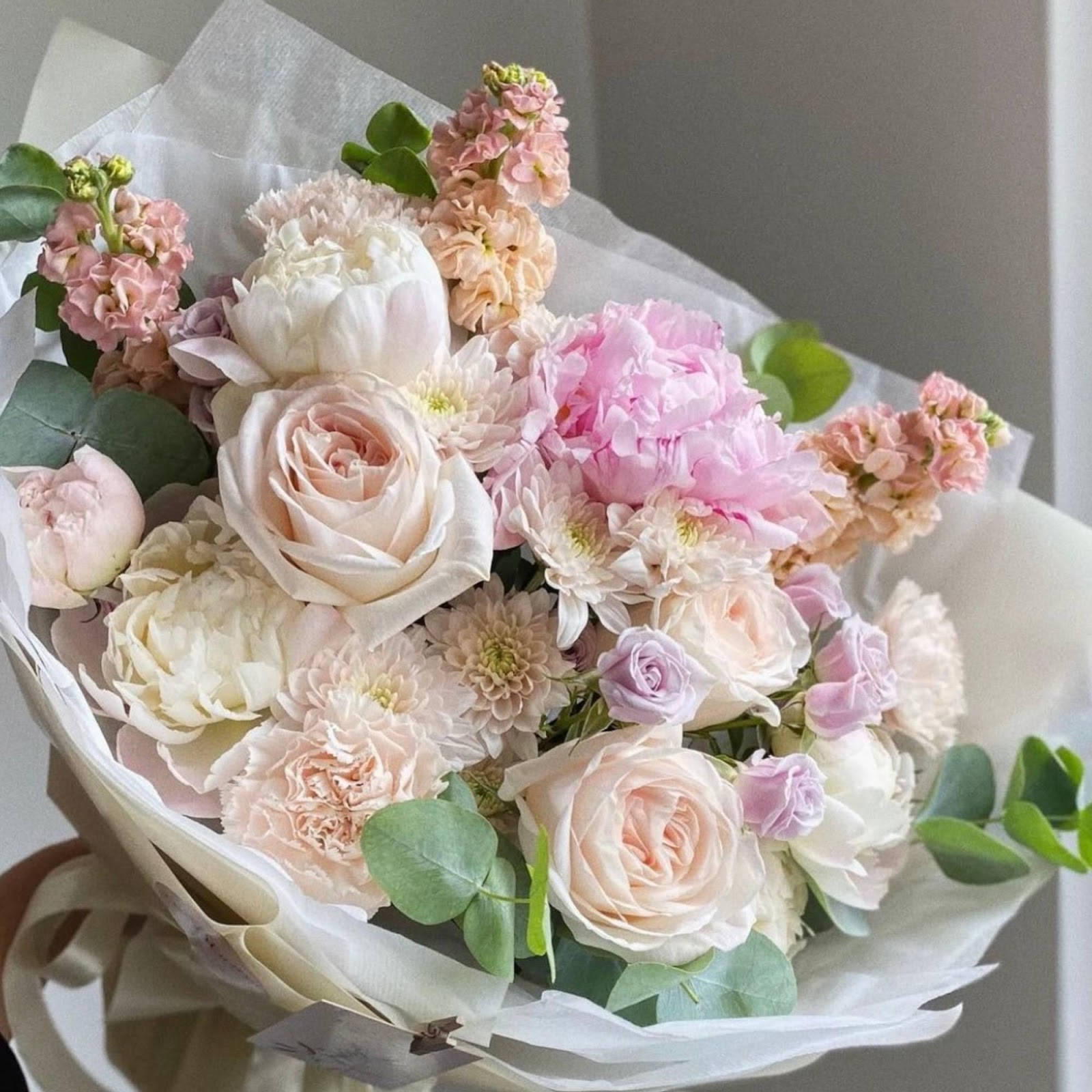 A vibrant floral arrangement featuring peonies, roses, matthiola, spray roses, carnations, and eucalyptus, creating a lush and colorful display with a variety of textures and shapes.