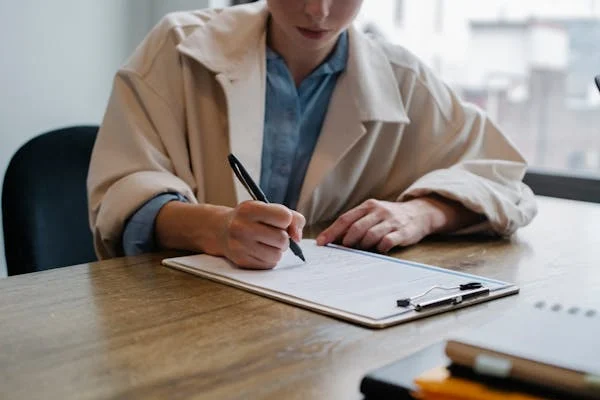 asian female employee wearing overcoat holding a pen and writing bereavement leave application