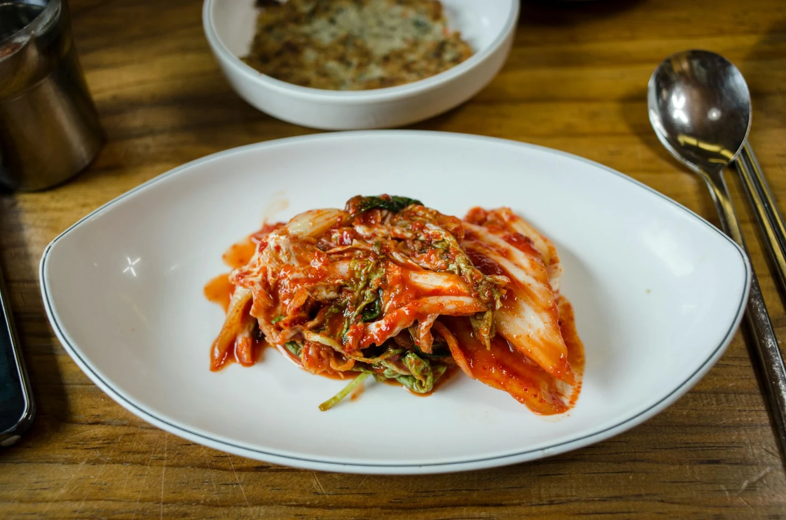 korean cusine kimchi in plate with spoon is placed on table.