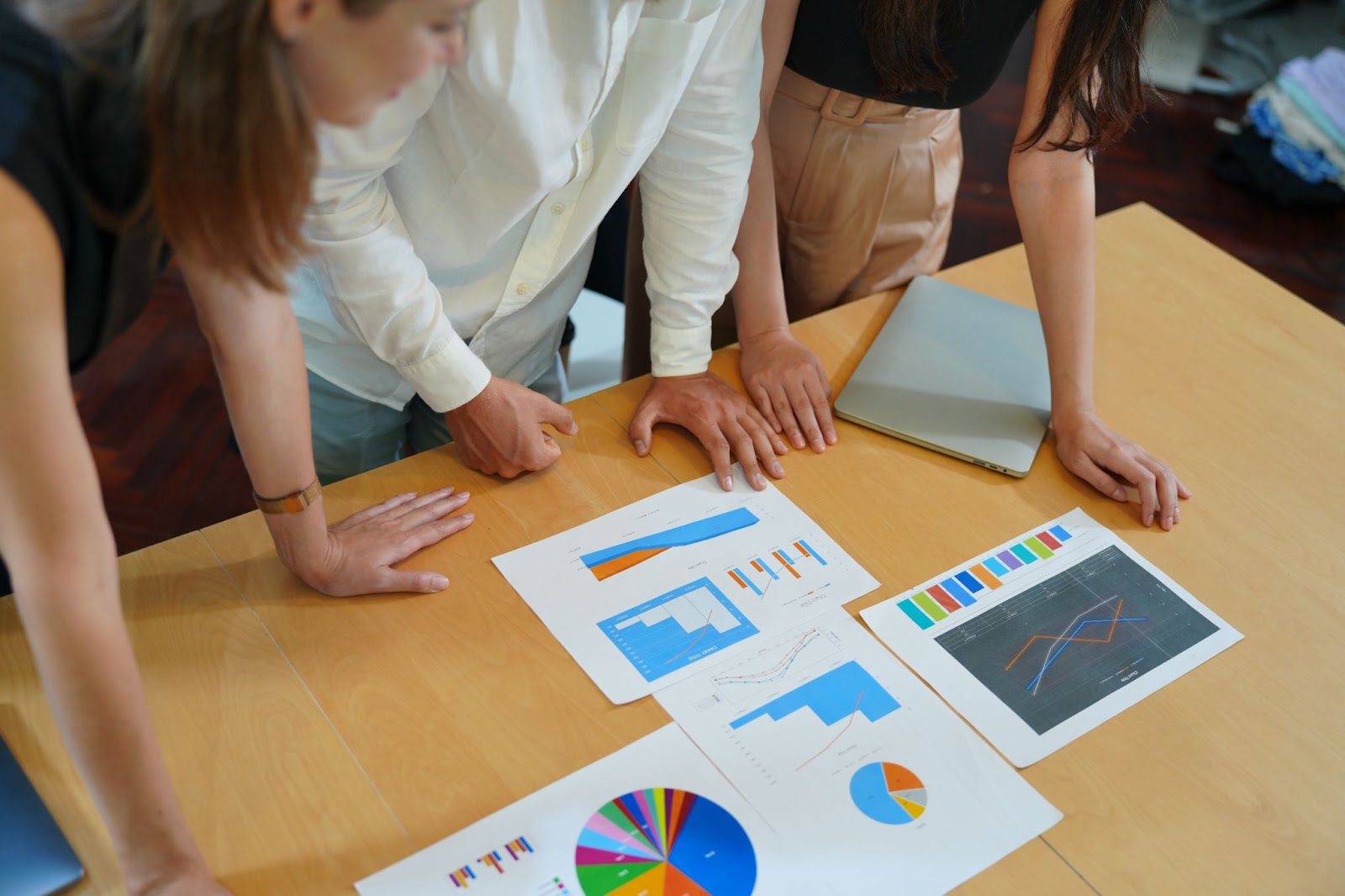 Two women and a man looking at data on pieces of paper on a wooden surface. 