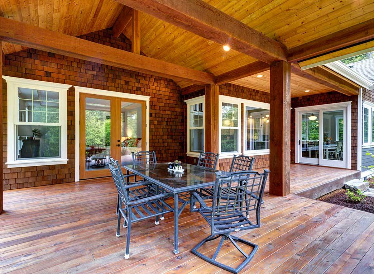 Rear covered deck crowned with a cathedral ceiling. It has a metal outdoor dining set and a french door that leads to the primary bedroom.