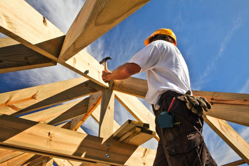 A person in a hard hat hammering a nail into a wooden beam
Description automatically generated