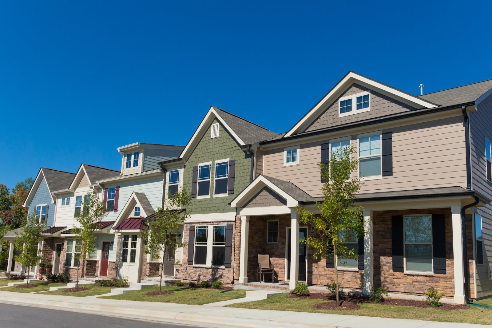 A row of modern houses with varied colors and architectural styles under a clear blue sky.