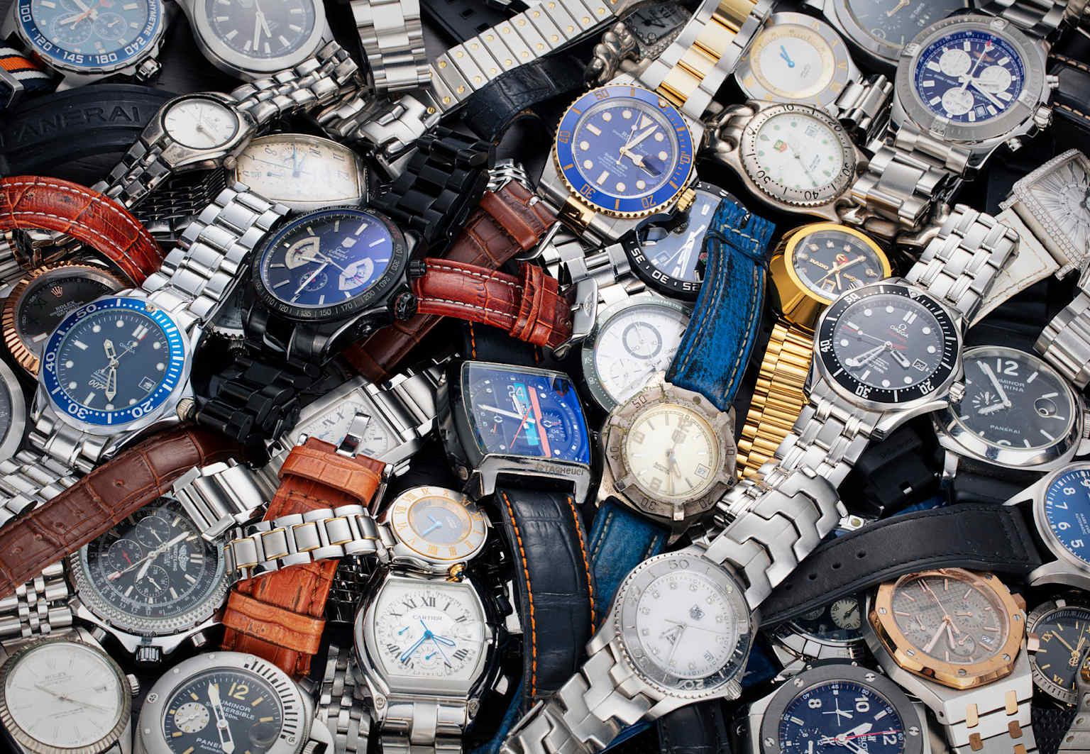 A pile of various wristwatches illustrating the risk of counterfeit or unverified pre-owned luxury watches