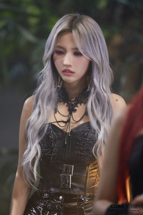 This contains a picture of  Soyeon with long grey hair standing in front of another person wearing black dress and necklaces