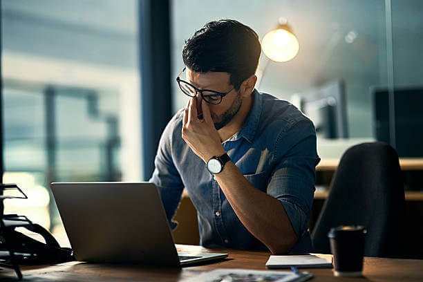 A man sitting at his desk with his head in his hands, looking overwhelmed, symbolizing the need for stress supplements to manage tension.