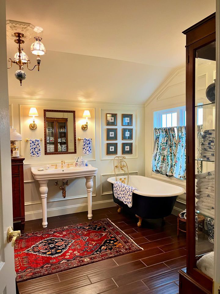 A spacious bathroom with a black clawfoot tub, floral curtains, a Persian-style rug, and a large white sink. 