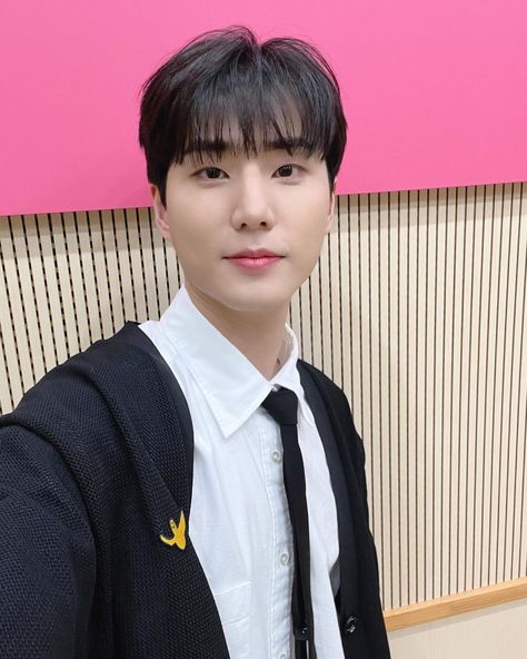 This contain  Young K  wearing a black tie and white shirt in front of a pink wall