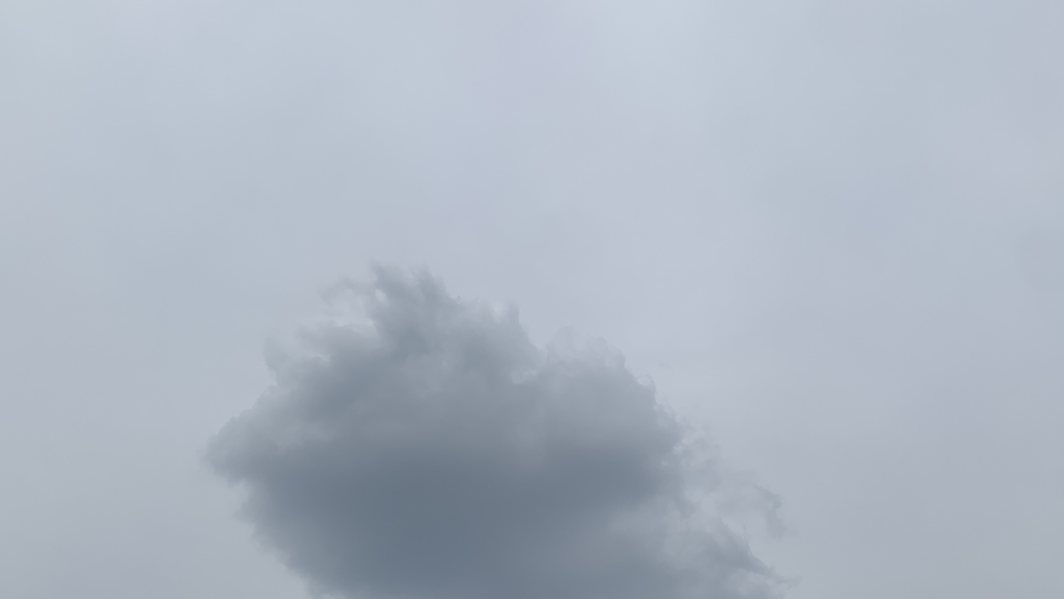 A gray puffball cloud way up close at the bottom of the frame in front of a dull light bluish-gray sky