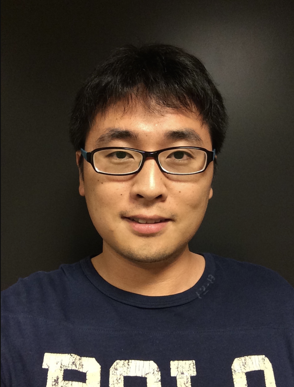 Portrait of Professor Zhang smiling, wearing a navy polo t-shirt.