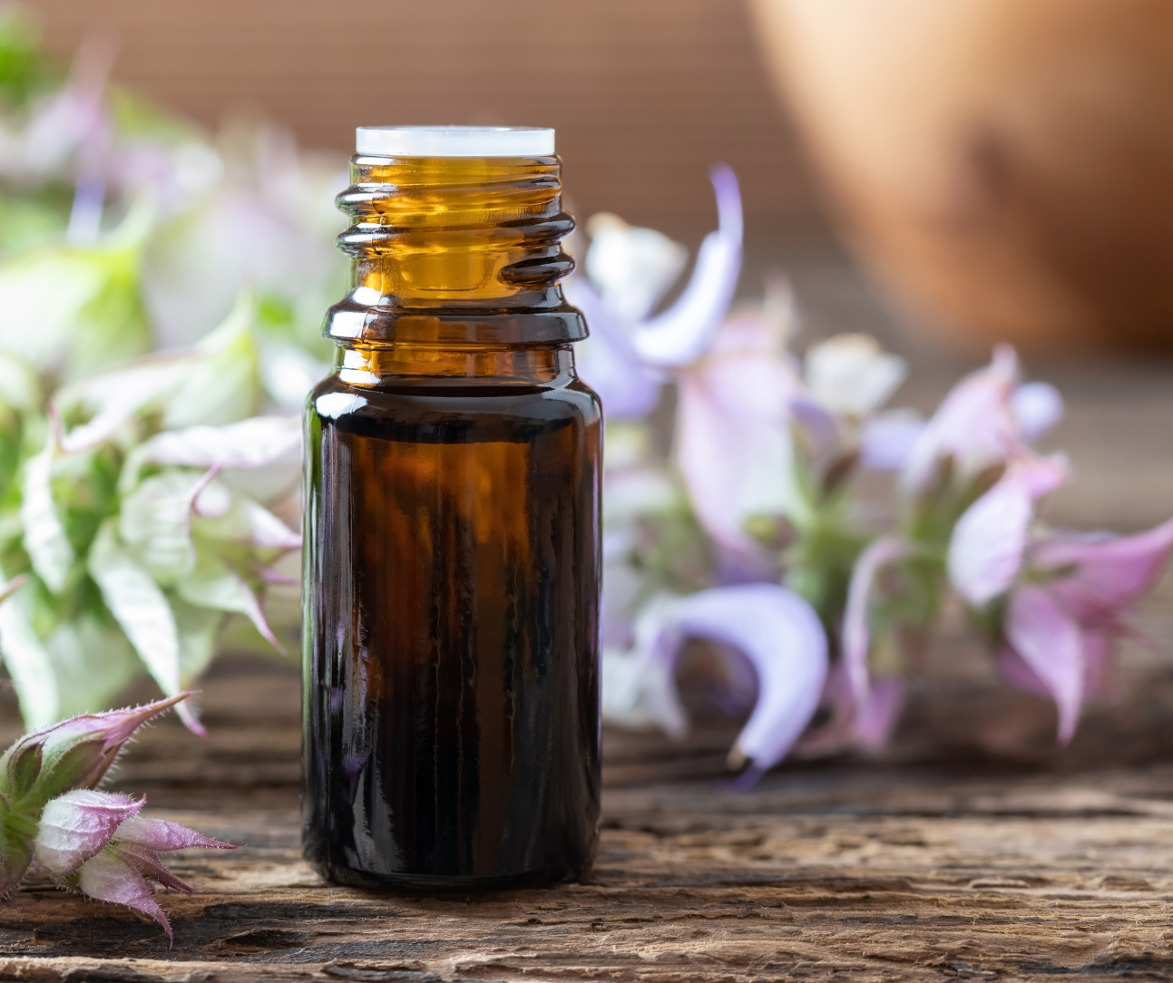 a bottle of essential oil and clary sage flowers