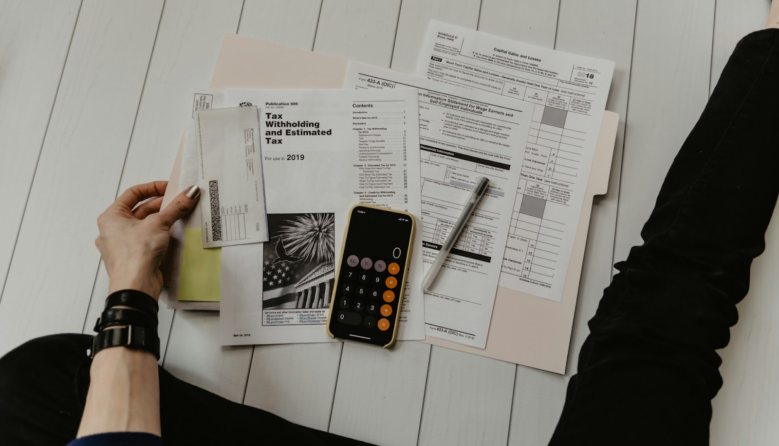 Person organizing tax documents and using a calculator to manage cash flows.