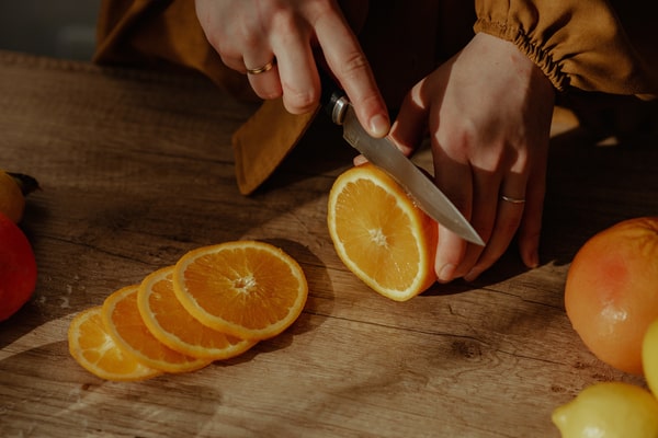 A person slicing an orange on a wooden surface