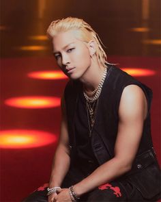 This containTaeyan with blonde hair sitting on a red floor wearing a black shirt and jeans