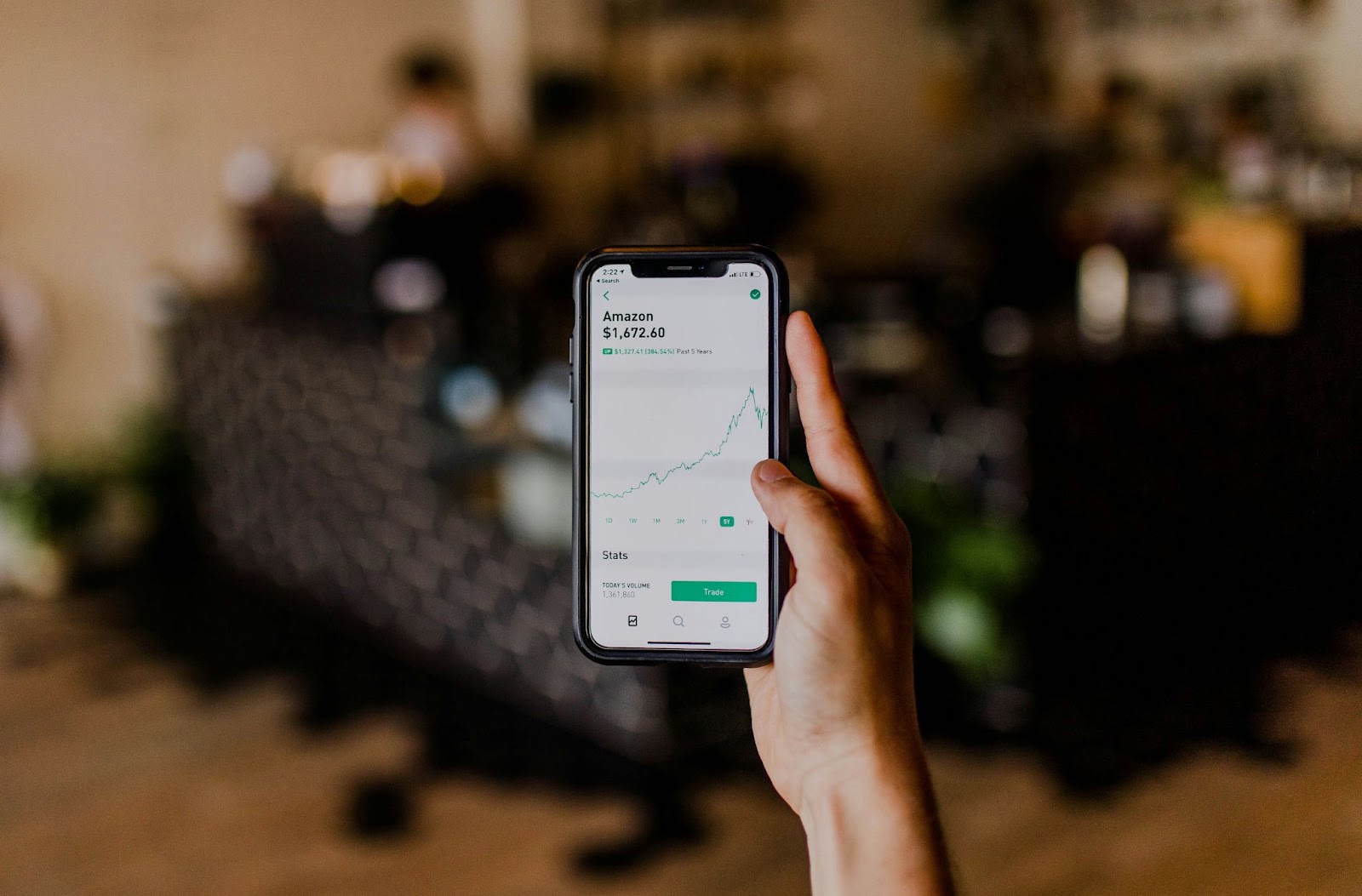 Person holding a phone displaying Amazon stock graph and stats on screen