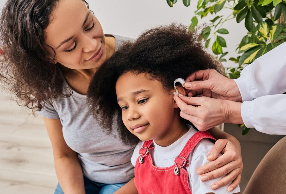 An Audiologist inserts a hearing aid into a child’s ear
