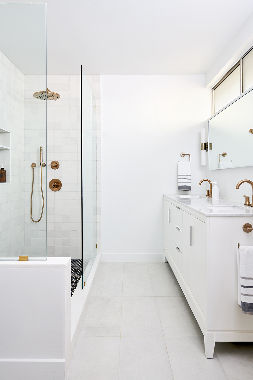 Transitional bathroom design with a white vanity, large format floor tiles, black hexagonal shower tile, and brass fixtures