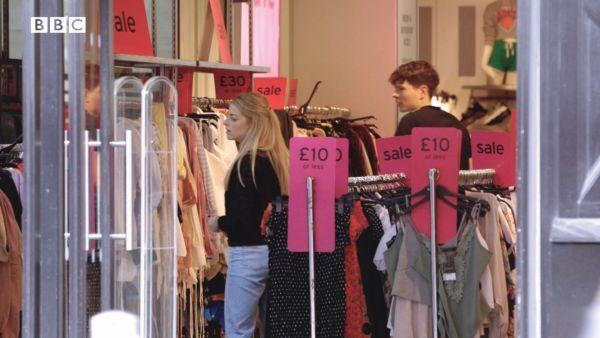 Letter A. People are shopping in a clothes store. There are many racks full of clothes and they are all on sale. The racks in the middle of the store feature clothes being sold for 10 pounds of less.