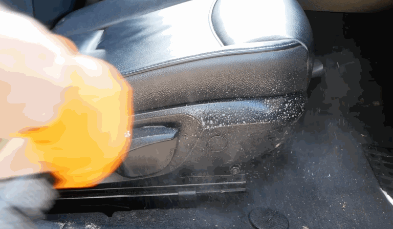 A handheld steamer cleaning the side panel of a car seat, emitting visible steam and breaking down dirt and grime effectively.