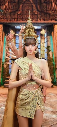 This contain an image of Lisa in a gold outfit standing next to a golden statue and wearing a crown