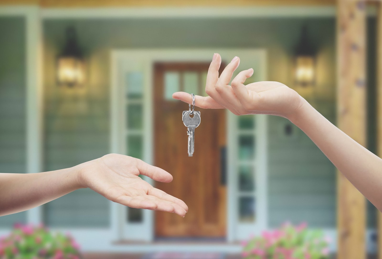 A hand is passing a key to another hand in front of a house entrance.