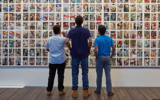 A group of people looking at a wall of picturesDescription automatically generated