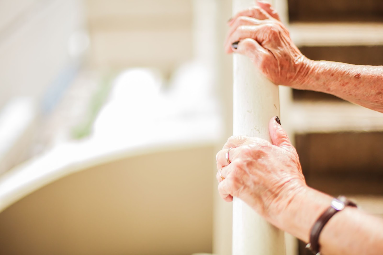 Close up older adult's hands holding a hand rail while using the stairs.