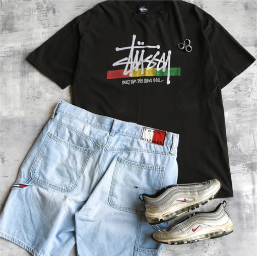 A laid-out thrifted outfit featuring a black graphic T-shirt, light-wash denim shorts, and silver Nike sneakers.