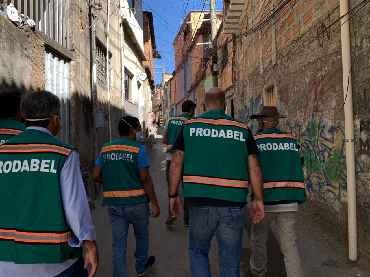 A group of men wearing green vests walking down a street</p>
<p>Description automatically generated