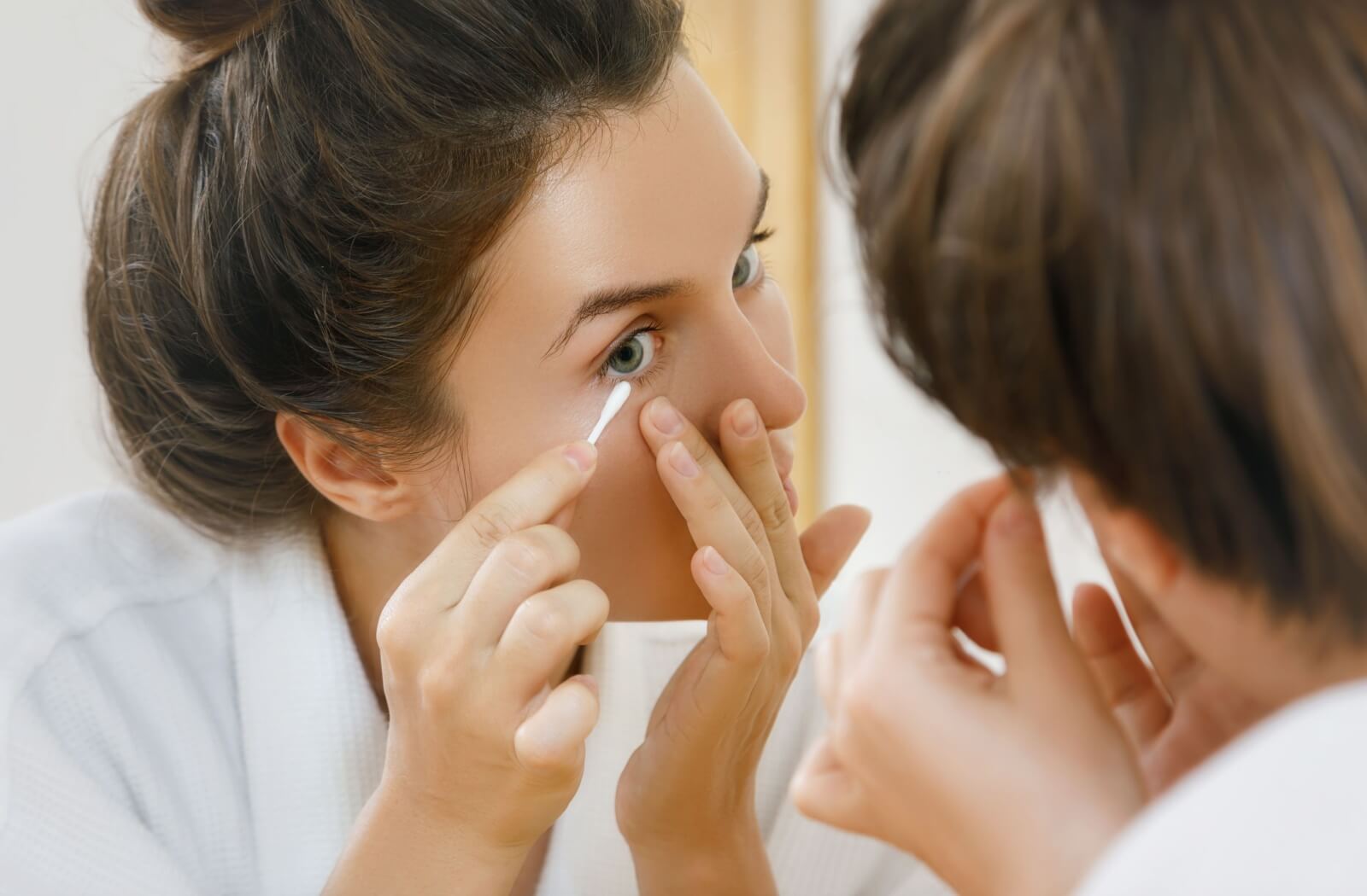 A person using a cotton swab gently cleans their eyelid to prevent infection.