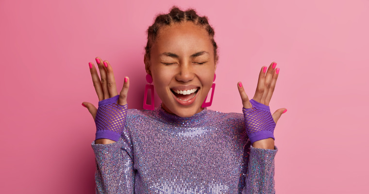 Mulher negra usando roupas roxas e exibindo seus tipos de esmaltação colorida. 