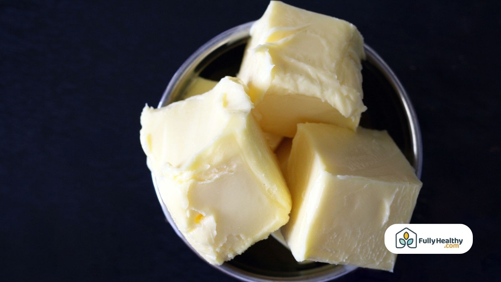Butter chunks in a metal bowl on dark background FullyHealthy logo