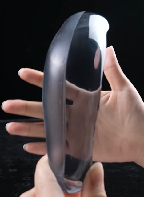 A hand holding a 3D-printed transparent resin object, partially sanded to show a contrast between the frosted, unpolished side and the smooth, crystal-clear polished side.